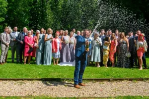 My signature photograph. A groom celebrates his wedding by spraying a bottle of champagne beside his bride and in front of his family and friends. Devon Wedding Photographer. GoodLuckPhotography