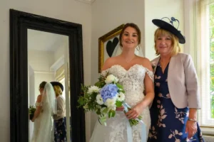 A bride stands with her mother, minutes before her wedding ceremony, relecting in the mirror beside them by Devon Photographer - Robb Webb