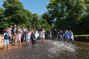 North Devon Photographer - Robb Webb Documentary wedding photographer standing barefoot in a flooded river during an outdoor wedding ceremony in the New Forest, Hampshire