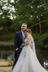Newlywed couple pose for photographs by a brook in the grounds of their country house hotel by Devon Photographer Robb Webb
