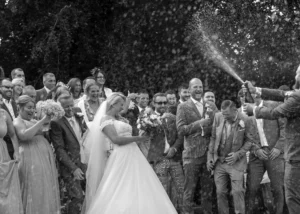 North Devon Photographer - Robb Webb Black and white wedding photograph of a groom spraying champagne over his bride and guests during a joyful celebration in Devon