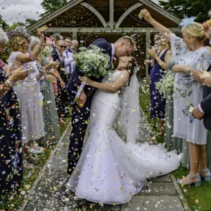 North Devon Photographer - Robb Webb Bride and groom kissing during a confetti exit at an outdoor North Devon wedding, photographed by Robb Webb Wedding Photographer
