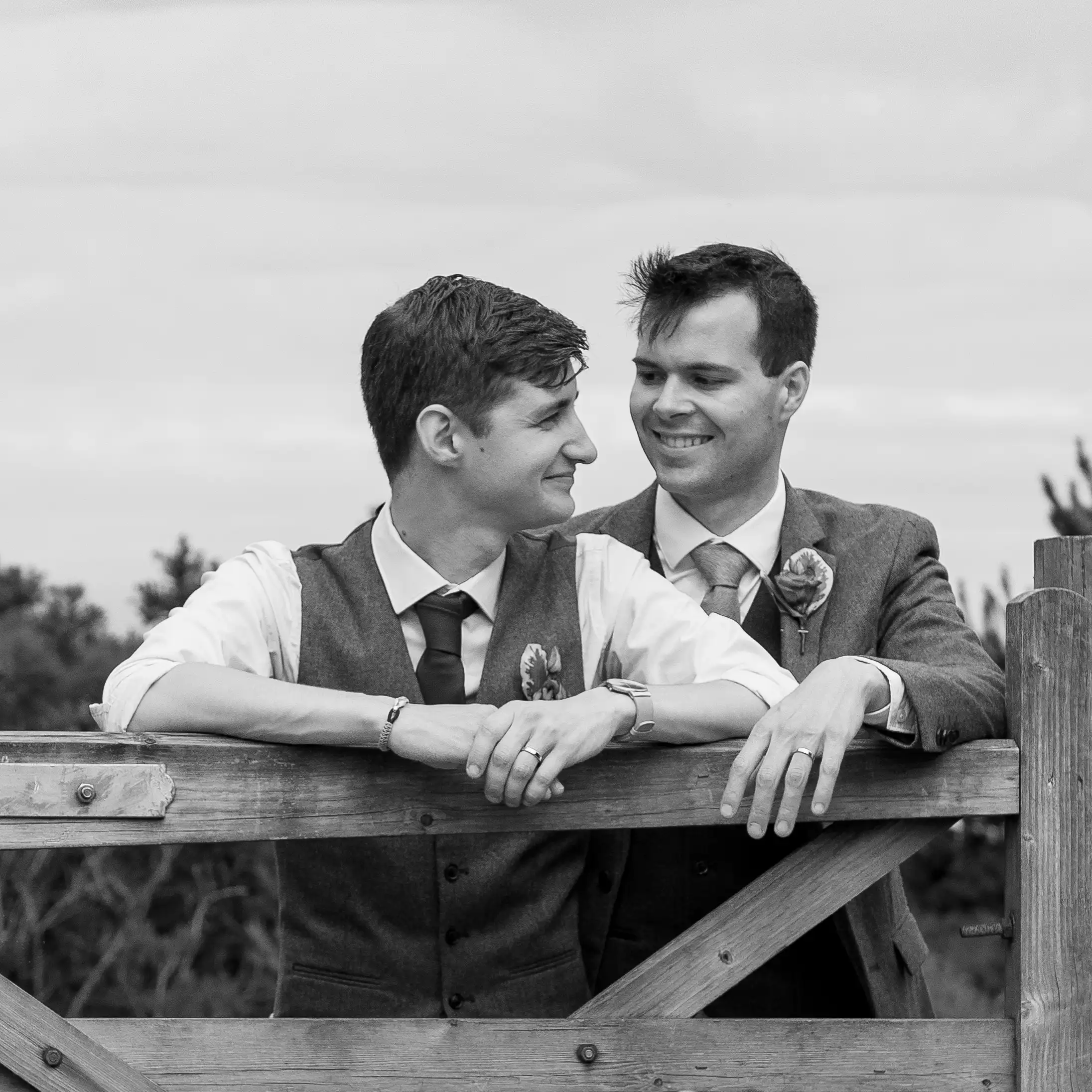 North Devon Photographer - Robb Webb A-black-and-white-picture-of-a-same-sex-couple-leaning-on-a-farmers-gate-Groom-and-Groom